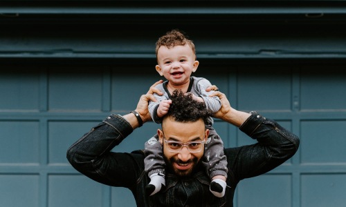 a man holding his son on his shoulders in front of a building
